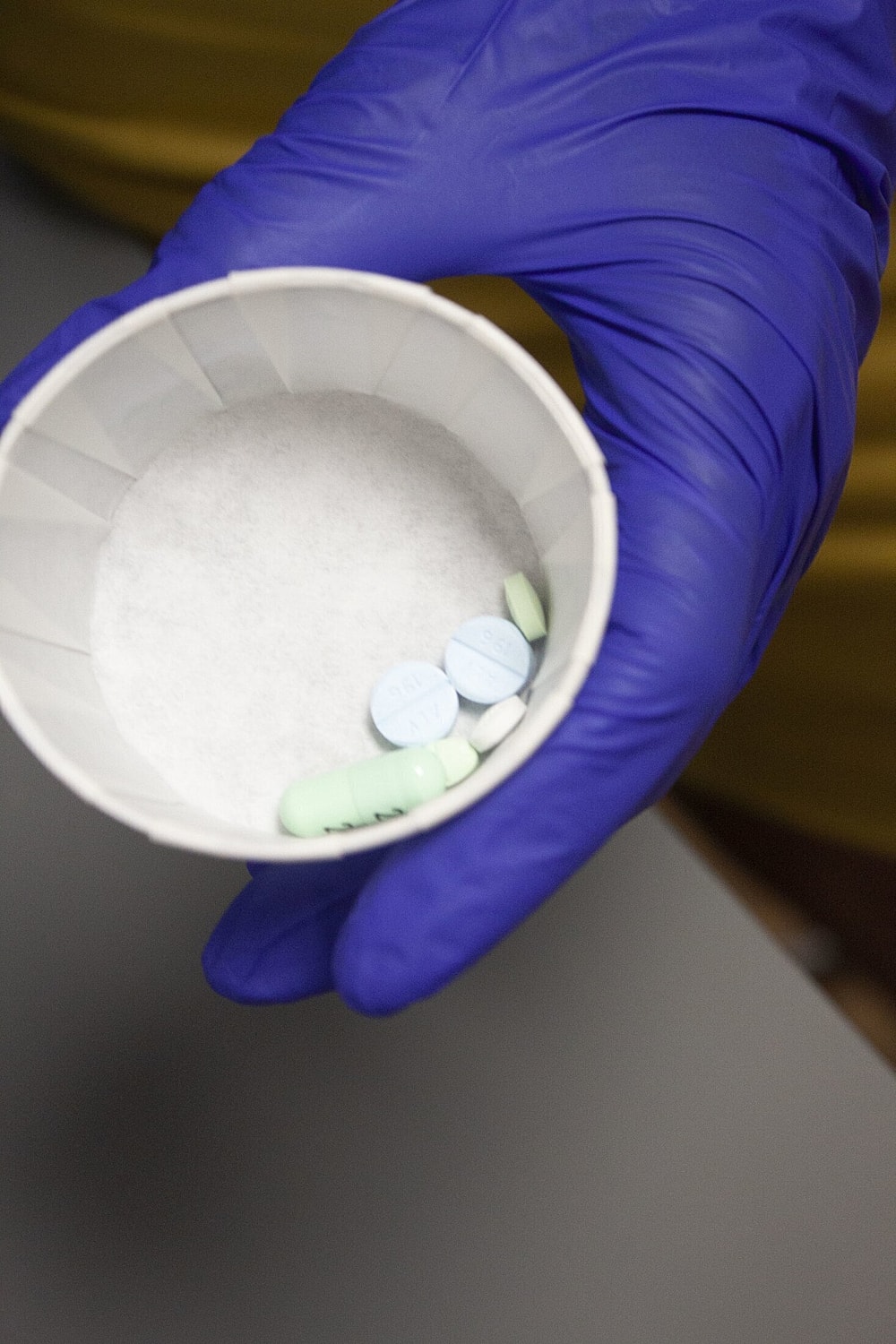 Gloved hand holding a cup of medication.