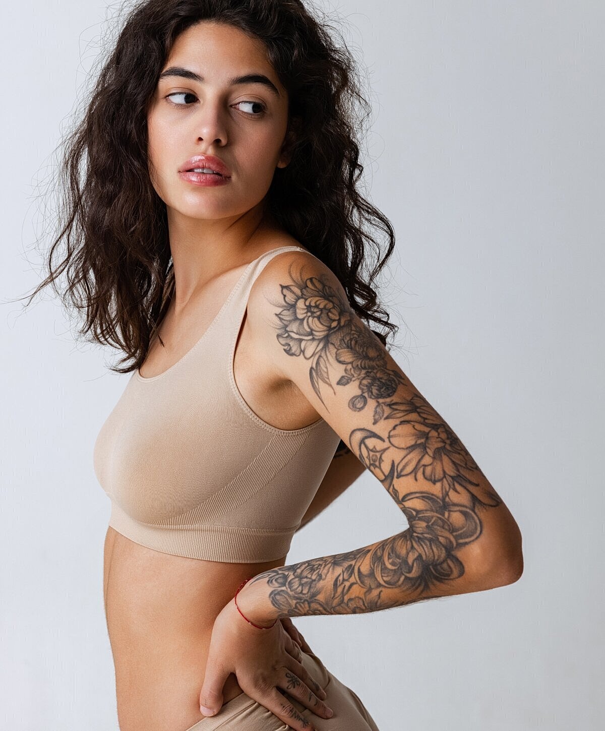 Woman with tattoos wearing a beige sports bra.