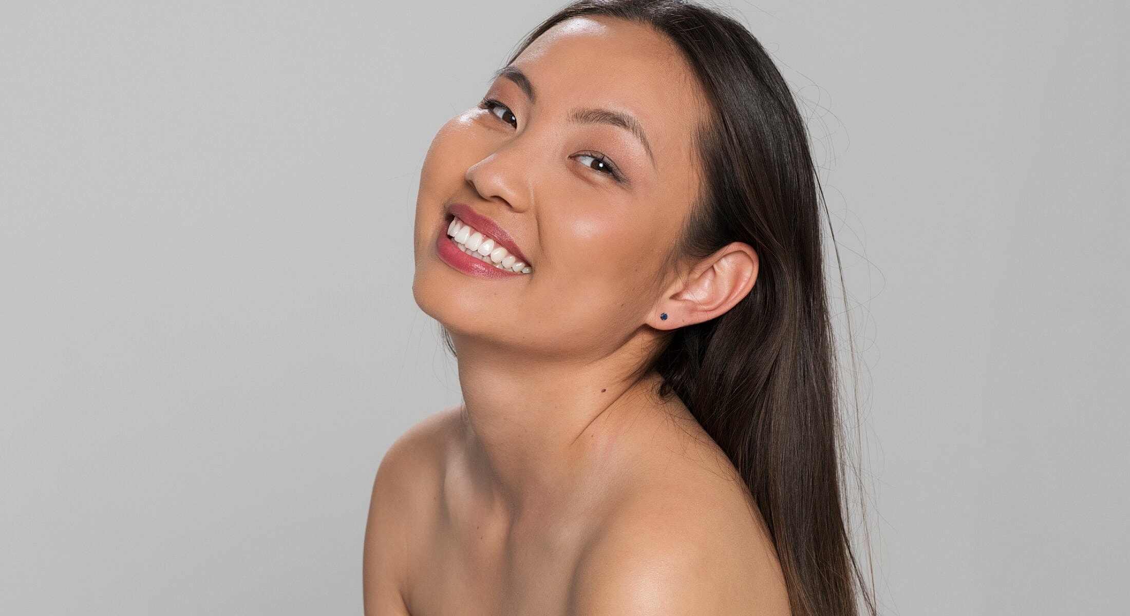Smiling woman with long hair against gray background.